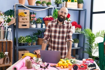 Young bald man florist smiling confident using laptop at flower shop