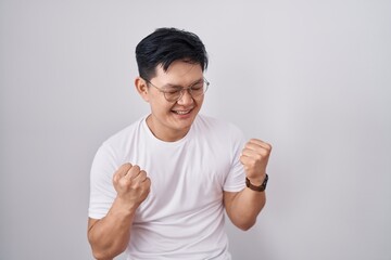 Young asian man standing over white background very happy and excited doing winner gesture with...