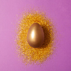 Minimal flat lay with golden egg and glitter on purple background. Creative easter concept.