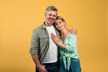 Portrait of happy mature couple hugging and posing at camera, middle aged spouses standing over...
