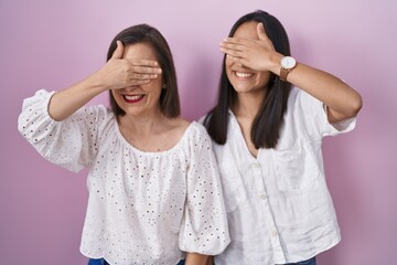 Hispanic mother and daughter together smiling and laughing with hand on face covering eyes for...