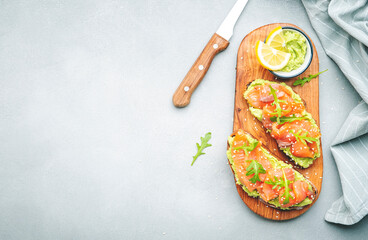 Avocado salmon sandwich or toast on rye bread with guacamole sauce, young arugula and sesame seeds, gray table background, top view copy space