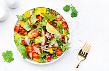 Fresh salad with grilled chicken slice with mango salsa, tomato, cilantro, red onion and lettuce in mexican style, white table background, top view