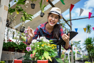 Modern technology in gardening business. Portrait of Asian female environmentalist using digital tablet in garden. Confident female is wearing apron while working.