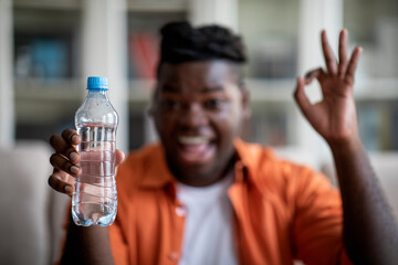 Obraz na płótnie Canvas Selective focus on bottle of water in black guy hand