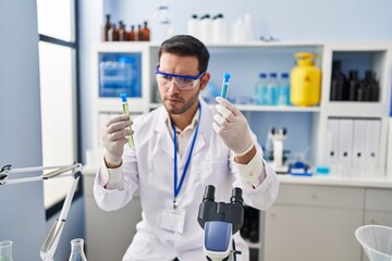 Young hispanic man scientist holding test tubes at laboratory