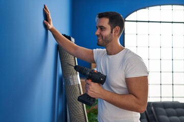 Young hispanic man smiling confident holding drill at new home