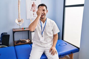 Young hispanic man with beard working at pain recovery clinic covering one eye with hand, confident...
