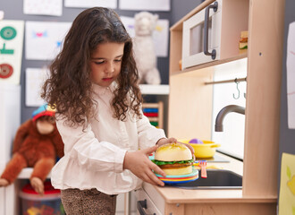 Adorable hispanic girl playing to cook hamburger toy with play kitchen at kindergarten