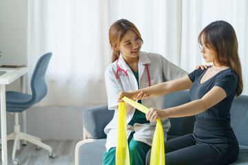 Asian woman physiotherapist oversees the patient’s stretching with elastic tape.