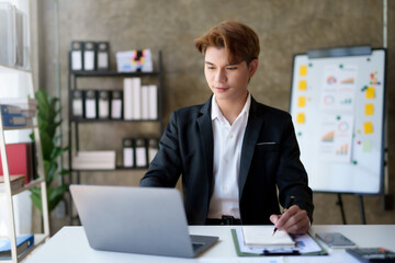 Young asian businessman sitting working with laptop computer in office.