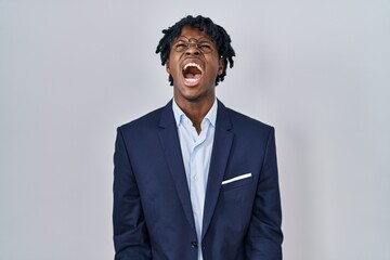Young african man with dreadlocks wearing business jacket over white background angry and mad screaming frustrated and furious, shouting with anger. rage and aggressive concept.