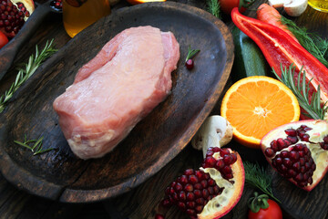Fresh, pink, pork pulp on a wooden plate and on a wooden table, spices, herbs, vegetables and fruits with marinade are carefully laid out around the pork.