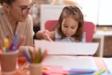 Teacher and toddler smiling confident cutting paper at kindergarten