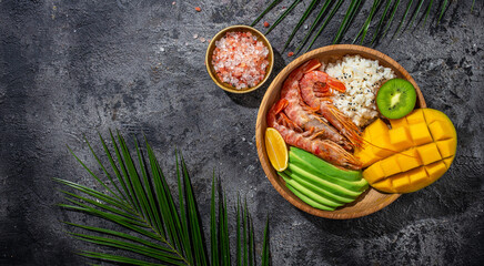 Poke with shrimp, avocado, rice, mango, kiwi and coconut. Hawaiian cuisine. Tropical food. Lunch on the beach. Long banner format. top view