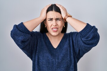 Young brunette woman standing over isolated background suffering from headache desperate and stressed because pain and migraine. hands on head.