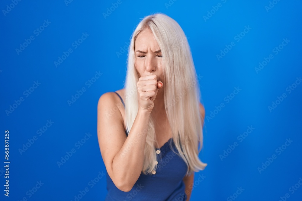 Poster caucasian woman standing over blue background feeling unwell and coughing as symptom for cold or bro