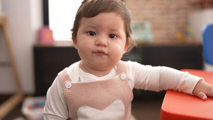 Adorable toddler standing with relaxed expression leaning on table at kindergarten
