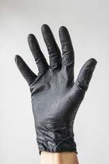 A hand in a black rubber glove on a white background. Personal protective equipment. A man's hand in a black latex glove on a white background close-up. Black gloves isolated on white. Vertical photo.