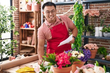 Young chinese man florist writing on notebook reading document at florist