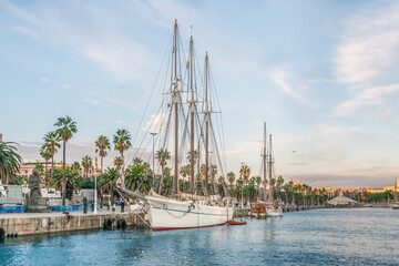 White sailing ship with three masts and lowered sails moored near the waterfront of Barcelona with...