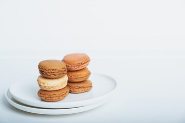 Stack of delicious freshly baked caramel, coffee and vanilla flavoured macaron confections on white plate against white background. Copy space for text. French sweet food speciality.