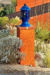 Fototapeta premium Light post in front yard with orange stucco exterior and slick blue lamp on top with light inside in desert environment