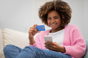Happy pretty black woman sitting on couch, making online order