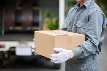 Mover with cardboard box standing in front of truck with opened