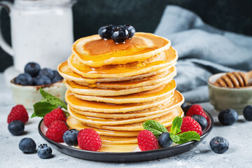 Delicious pancakes, with fresh blueberries, raspberry and maple syrup or honey on a dark background