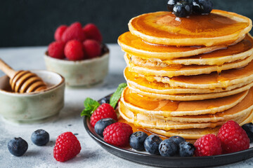 Delicious pancakes, with fresh blueberries, raspberry and maple syrup or honey on a dark background