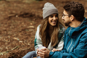 Happy young european man and female tourists in jackets rest in autumn forest, enjoy cold season outdoor