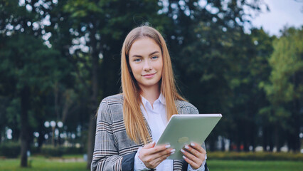Fototapeta premium A young girl walks with a tablet in the park.