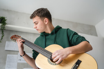 One young man Caucasian teenager sit at home in room playing guitar - obrazy, fototapety, plakaty