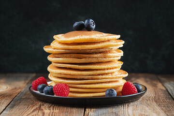 Delicious pancakes, with fresh blueberries, raspberry and maple syrup or honey on a dark background