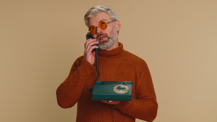 Bored tired middle-aged old man talking on wired vintage old-fashioned telephone of 80s, fooling...