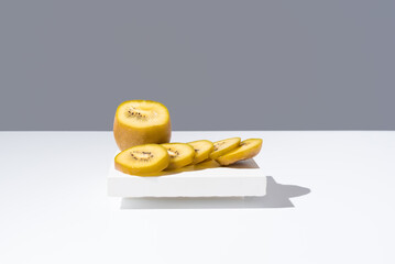 Rebanadas de kiwi amarillo dorado sobre un soporte blanco y fondo gris