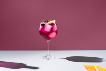 Copa de coctel de bayas rojas con trozos de naranja sobre fondo granate	