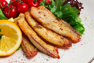 Fried Tilapia fish fillet, in spices, with cherry and salad, on a white plate, homemade, no people,