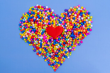A large heart of bright multicolored round candies, dragees on a blue background. Sugar candies. A...