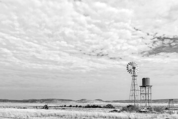 Water-pumping windmill and water tank on farm. Monochrome