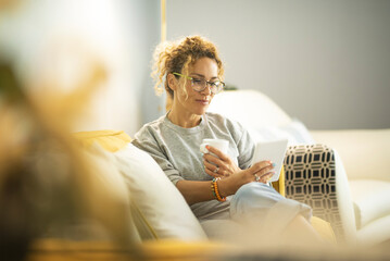 Smiling middle-aged Caucasian woman sit on couch in living room browsing wireless Internet on...