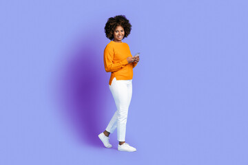 Fototapeta na wymiar Pretty black woman using cell phone and smiling on purple