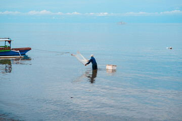 Old fisherman throws nets for fish on the beach