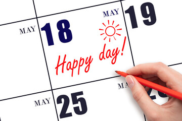 Hand writing the text HAPPY DAY and drawing the sun on the calendar date May 18