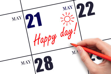 Hand writing the text HAPPY DAY and drawing the sun on the calendar date May 21