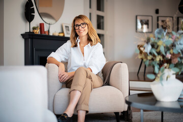 Attractive middle aged woman relaxing in an armchair in a modern home