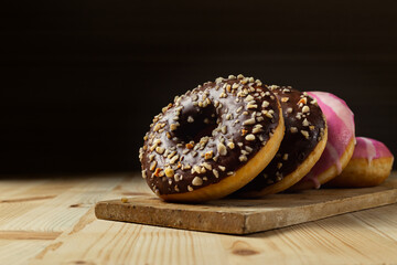 Close up of donuts with chocolate and pink frosting over a wooden table and dark background