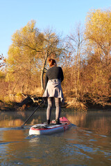 Woman paddle on stand up paddle board (SUP) at the morning on quiet river near shore with autumn...