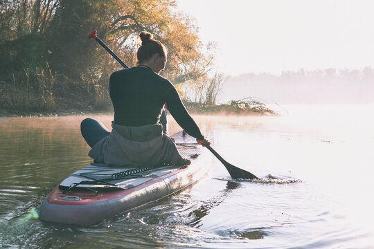 Woman Sitting On Stand Up Paddle Board (SUP) At The Morning On Quiet Misty River At Autumn